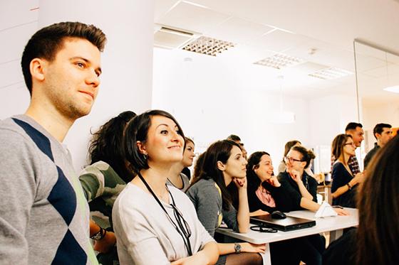 Photo of a group of professionals standing and sitting in a conference room, looking toward an off-frame speaker.